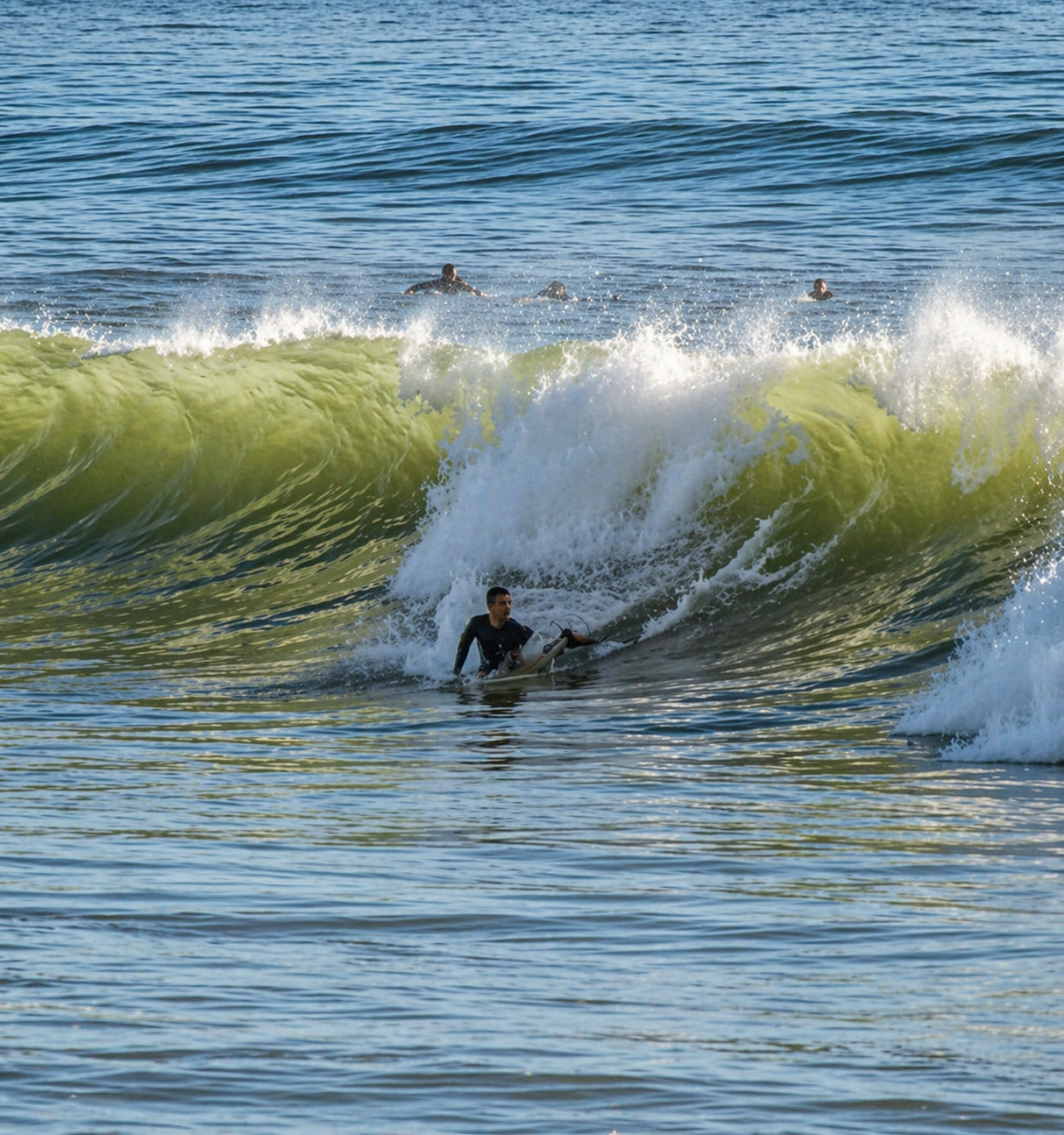 Surfer paddling out into a clean green wave at Praia de Faro