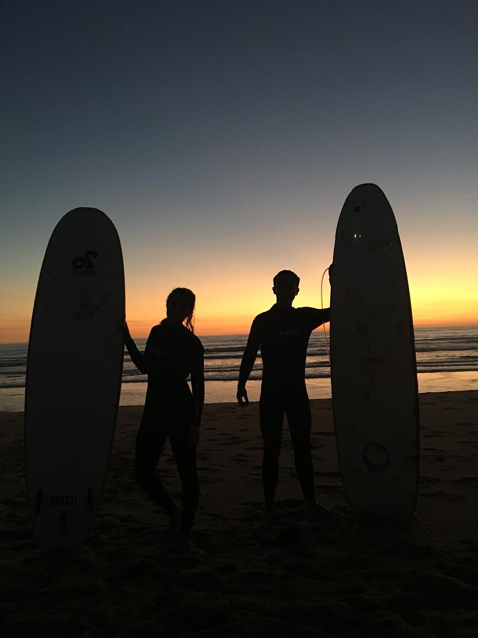 Surfers with boards silhouetted at sunset on Praia de Faro
